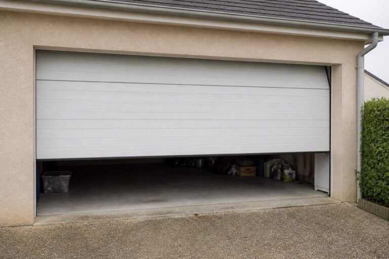Porte de garage sectionnelle blanche à moitié ouverte sur une maison individuelle