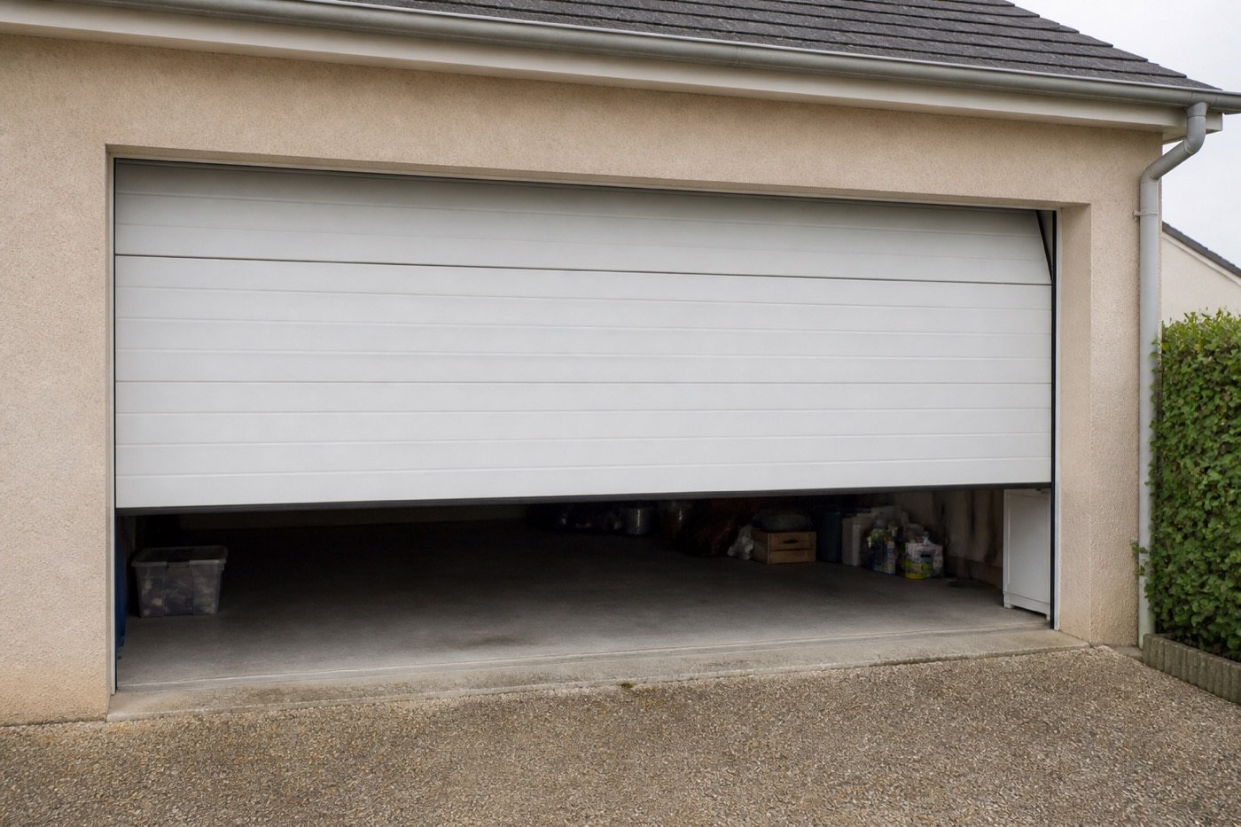 Porte de garage sectionnelle blanche à moitié ouverte sur une maison individuelle