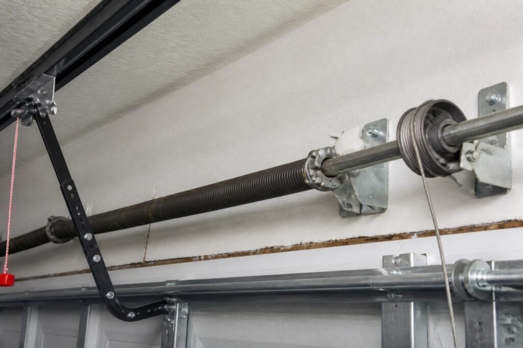 Ressort de torsion et tambour de câble fixés au-dessus d'une porte de garage sectionnelle, vus de l'intérieur